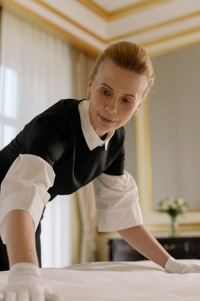 about-02 A housekeeper in uniform skillfully arranges bed linen in a luxurious hotel room.